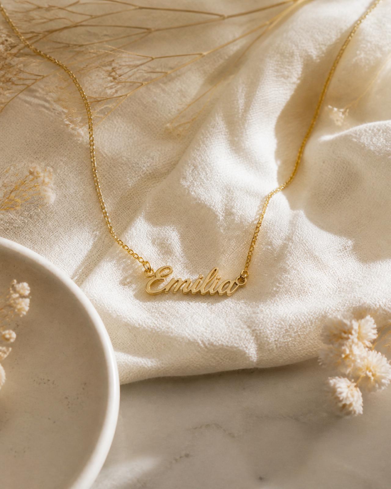 Personalized gold name necklace resting on soft ivory linen with dried florals